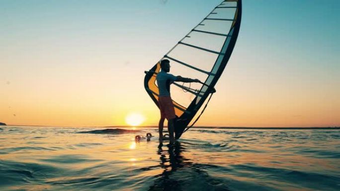 男人在夕阳下沿着湖边滑浪风帆