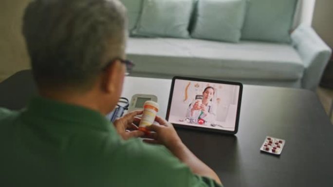 高级男子在家中与客厅的女医生在数字平板电脑上进行远程视频通话远程医疗会议