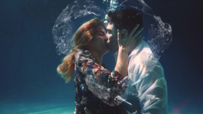 年轻无忧无虑的浪漫情侣的电影镜头是在蓝光水下激情接吻，水花呈心形。爱情、关系、自由、性感、幻想的概念