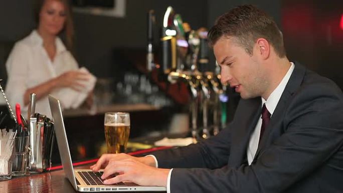 认真的商人在喝啤酒时在笔记本电脑上工作