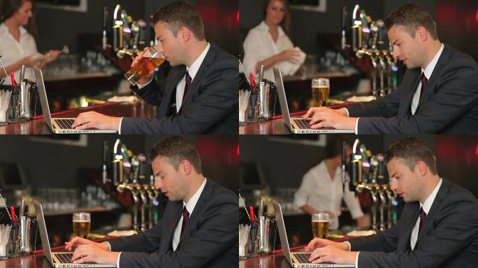 认真的商人在喝啤酒时在笔记本电脑上工作
