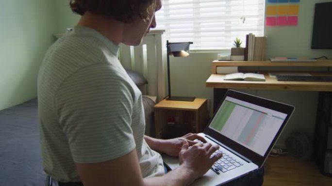 专注的高加索残疾人在卧室里使用笔记本电脑坐在轮椅上