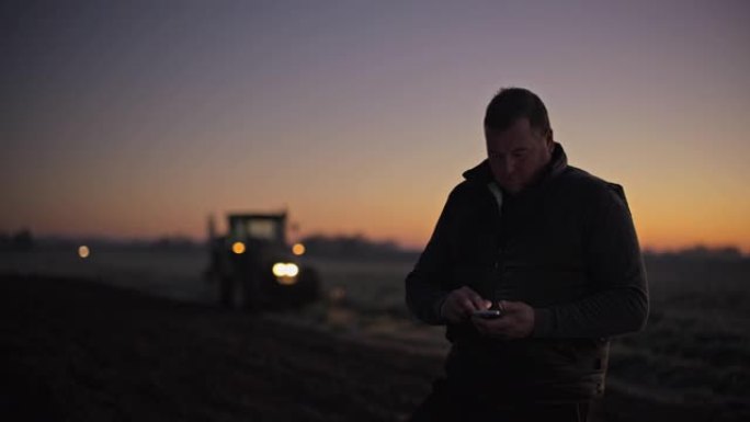 日出时在农村田地使用智能手机的肖像男农民