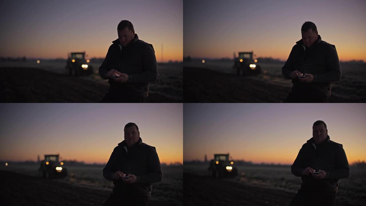 日出时在农村田地使用智能手机的肖像男农民