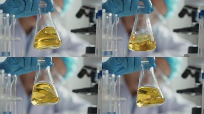 科学家戴着手套握住带有黄色液体的无菌烧瓶