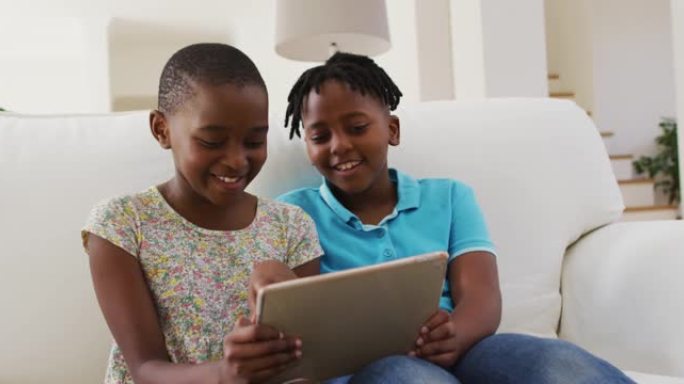 非裔美国男孩和女孩坐在家里的沙发上使用数字平板电脑