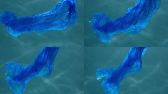 被塑料污染的海洋。特写蓝色一次性袋在光线背景下漂浮在水下慢动作。