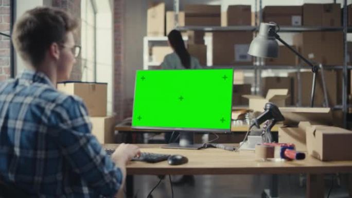年轻人使用带有绿屏Chromakey模拟显示器的台式计算机。销售经理和在配送仓库工作的员工用纸箱。肩