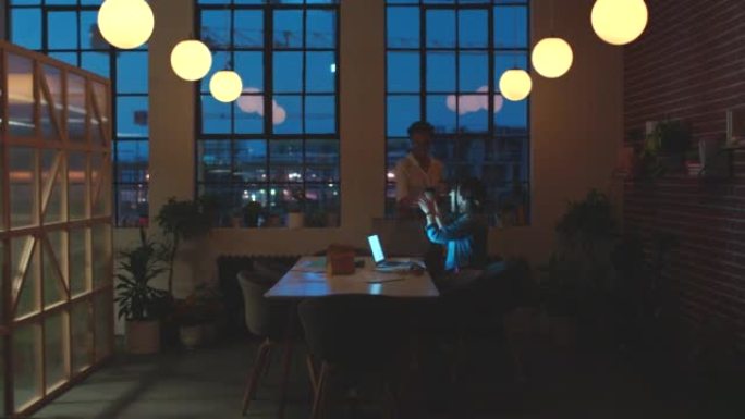 夜间计划，咖啡会议和女性在营销策略方面的沟通，在笔记本电脑上进行研究以及在黑暗办公室中合作。创业时商