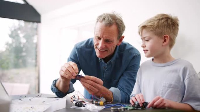 孙子与祖父组装电子元件在家中一起建造机器人