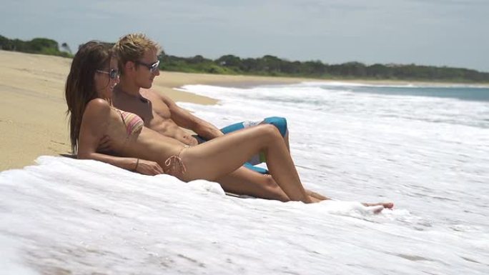慢动作: 年轻夫妇躺在浅水中的海滩上