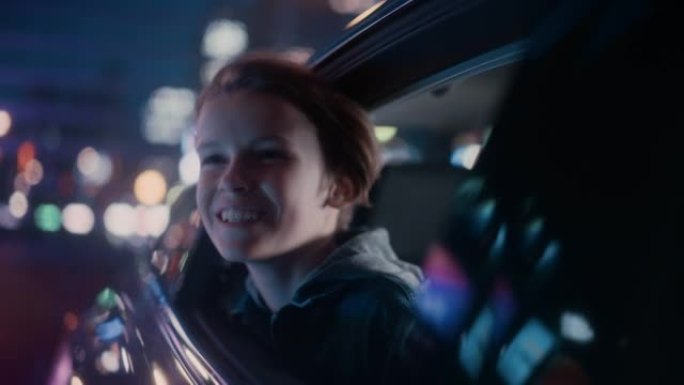 兴奋的小男孩坐在汽车后座上，晚上通勤回家。看着窗外，惊讶地发现带有工作霓虹灯的城市街道多么美丽。电影