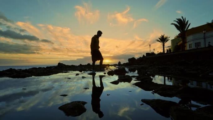 WS剪影，一名男子在水中的岩石上行走，并在水中倒影/西班牙加那利群岛