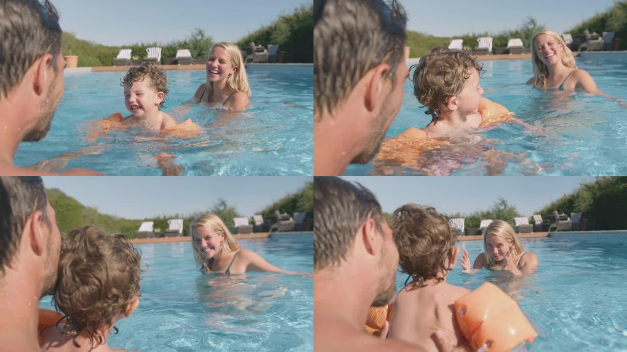 父母教儿子暑假在带充气臂章的室外游泳池游泳