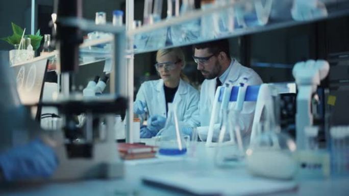 女性和男性医学研究科学家在用生物DNA样本进行试管和烧杯实验时进行了交谈。现代科学实验室。
