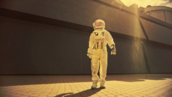 一位自信英俊的宇航员的低角度镜头正从工业金属墙走向相机。暖棕褐色颜色校正。穿着未来派西装的人，手上有