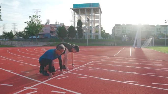 亚洲中国高级男子和他的儿子在起跑线上排队，准备清晨在田径体育场的男子跑道上跑步。