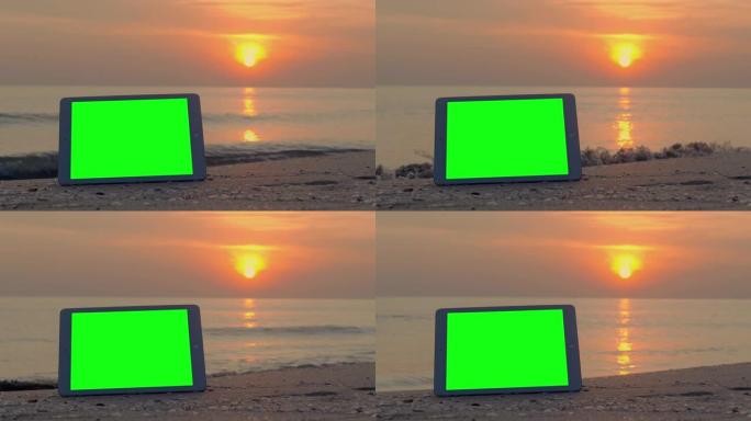 绿屏平板电脑和海滩上的跟踪点，而红色日落在度假背景下。新技术概念的绿屏。