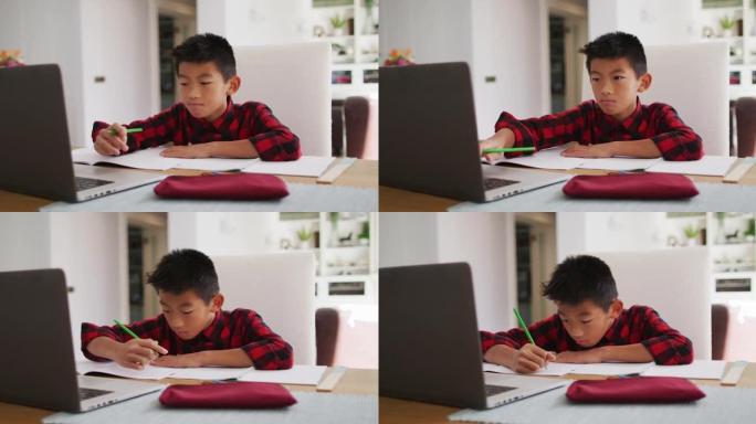 亚洲男孩在家，坐在桌子上使用笔记本电脑上在线学校课程
