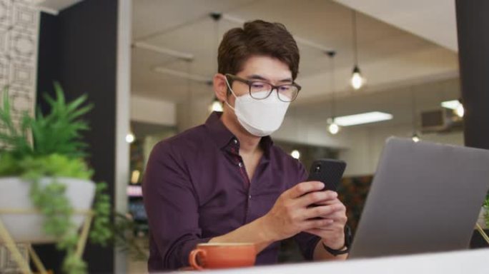 亚洲男子坐在咖啡馆时使用智能手机戴着口罩