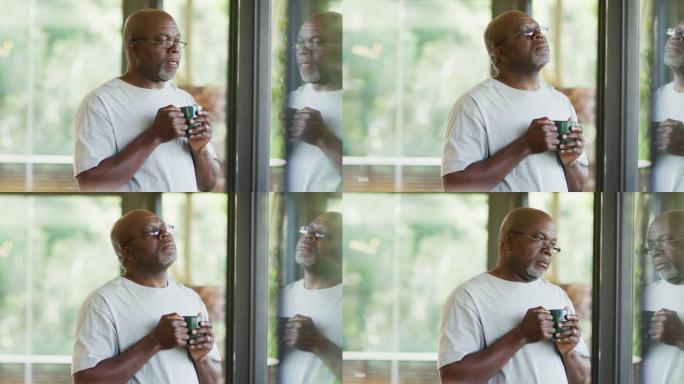 体贴的非洲裔美国老人站着喝杯咖啡，看着窗外