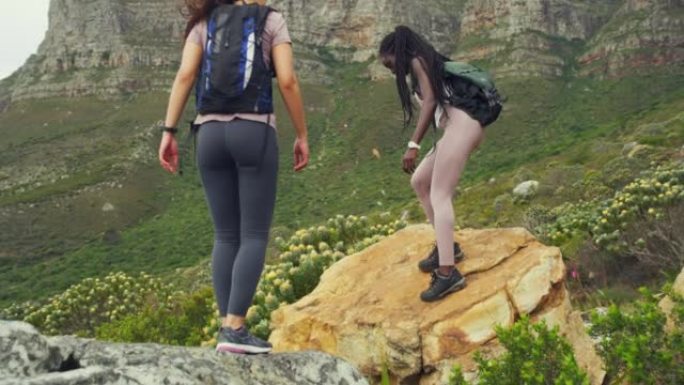 两个快乐的女人在大风天徒步爬上落基山。活跃的女性在自然公园攀爬和跳跃运动。穿着运动服的女运动员一起在
