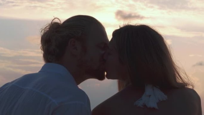 拉丁美洲和西班牙裔25-29岁夫妇的剪影，在沙滩上沿着日落海的边缘坐着和浪漫亲吻。假期-iStock
