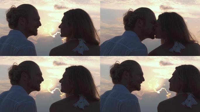 拉丁美洲和西班牙裔25-29岁夫妇的剪影，在沙滩上沿着日落海的边缘坐着和浪漫亲吻。假期-iStock