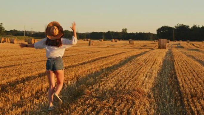 SLO MO年轻女子在满是草捆的田野上奔跑时丢了帽子