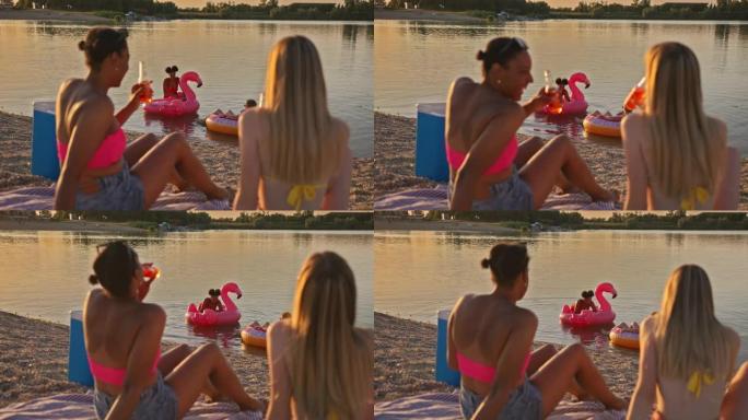 SLO MO两个年轻女人在沙滩上喝酒，而另外两个女人则在游泳花车上休息