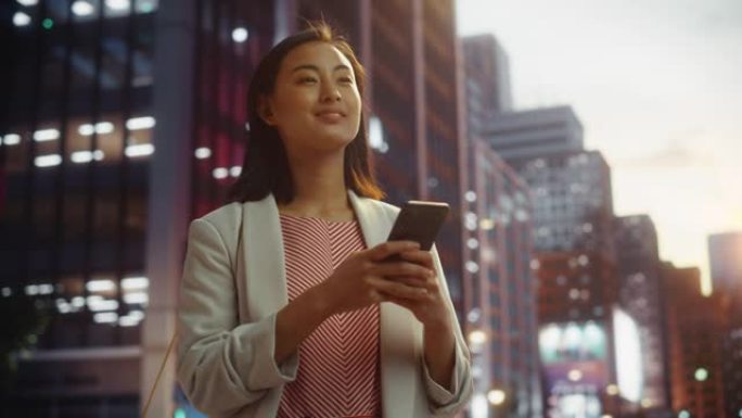 一位美丽的日本女性在日落时穿着时髦的休闲服并使用智能手机的肖像。时尚的女人在网上与人联系，传递信息和