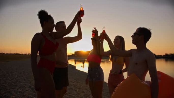 SLO MO一群年轻朋友在黄昏时在海滩上用冷饮敬酒