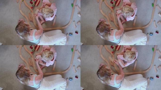母亲和女儿在家里的头顶镜头在地毯上玩木制火车玩具