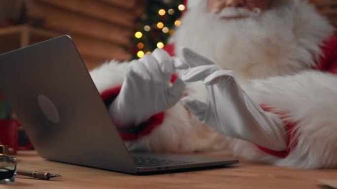 圣诞老人戴着白手套的手的特写镜头，在笔记本电脑上进行视频聊天时打手势