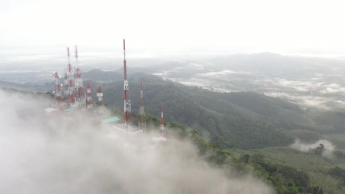 飞行无人机的鸟瞰图，具有4g和5g电信塔通信基站和天线的视差运动，在山顶上，禁食的云雾笼罩着泰国的绿