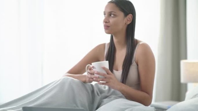 4k视频片段，一名年轻女子使用笔记本电脑并在家中床上喝咖啡