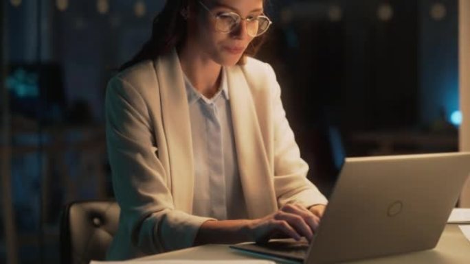 深夜在办公室工作的年轻会计师的特写肖像。积极的女性使用笔记本电脑，为财务总监准备工作分配和公司报告。