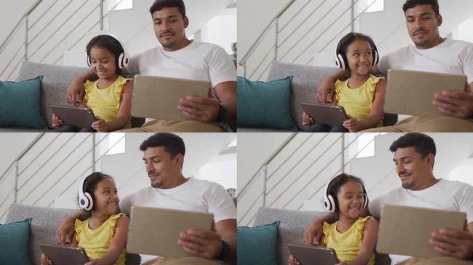快乐的西班牙裔父亲和女儿坐在沙发上使用平板电脑