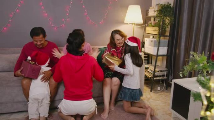 亚洲家庭祖父母在圣诞节期间与家人在家里的客厅庆祝时，向可爱的兄弟姐妹赠送惊喜礼盒。四个兄弟姐妹拥抱和
