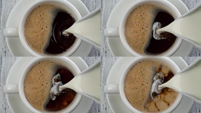 早餐时间-在带有泡沫的黑咖啡中添加牛奶。将牛奶倒入咖啡杯中。复古白色木质背景。自上而下的慢动作镜头