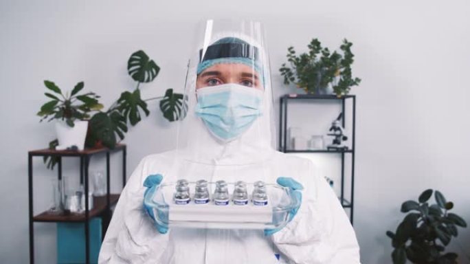 疫苗研究。严肃的女实验室科学家在防护服和盾牌上拿着治疗瓶以防冠状病毒。