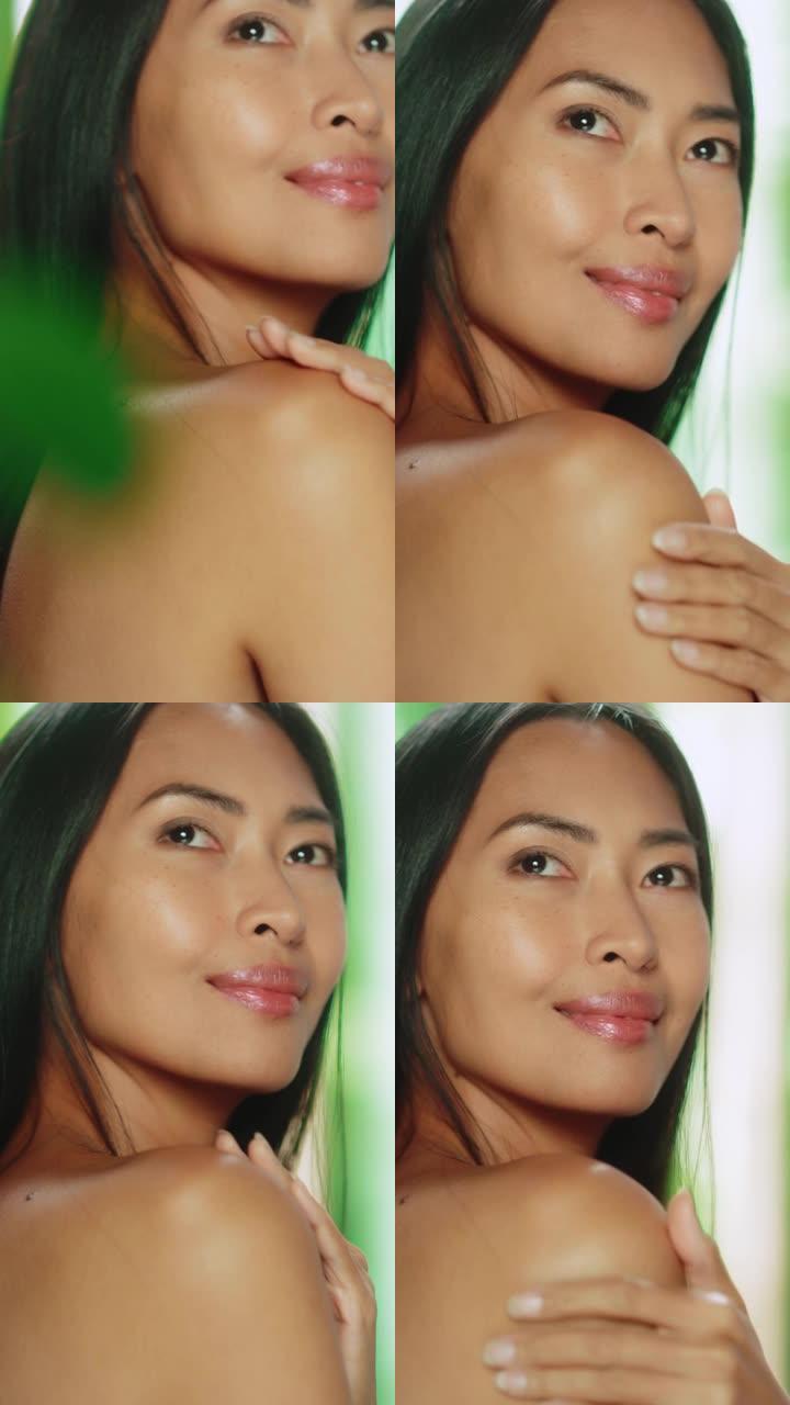 垂直屏幕。美丽的亚洲女人抚摸着她完美柔软的肩膀，脖子，性感地微笑。享受她美丽的女性。有机化妆品护肤品