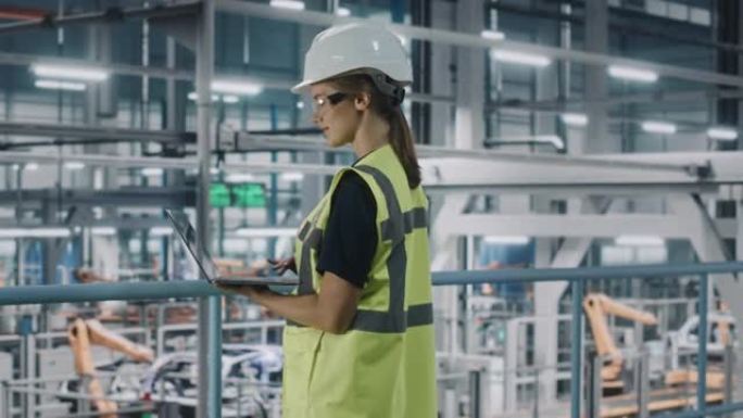 女汽车厂工程师穿着高能见度背心，使用笔记本电脑。汽车工业制造工厂致力于机器人技术的车辆生产。自动化装