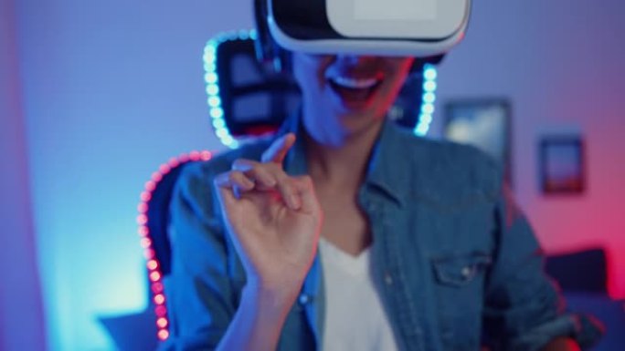 快乐亚洲女孩戴着虚拟现实眼镜护目镜耳机感觉惊喜真实游戏程序在她的霓虹灯家庭工作室晚上。