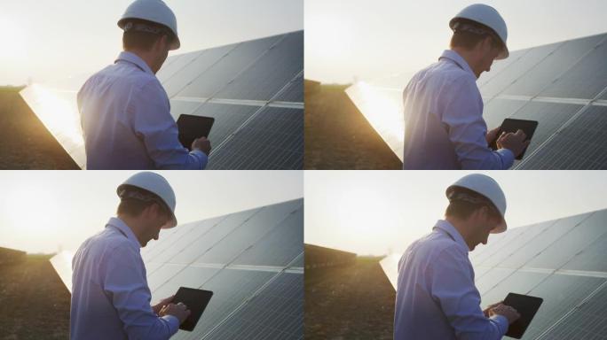 一位年轻的工程师正在用平板电脑检查日落时光伏太阳能电池板现场的阳光和清洁度。概念: 可再生能源、技术