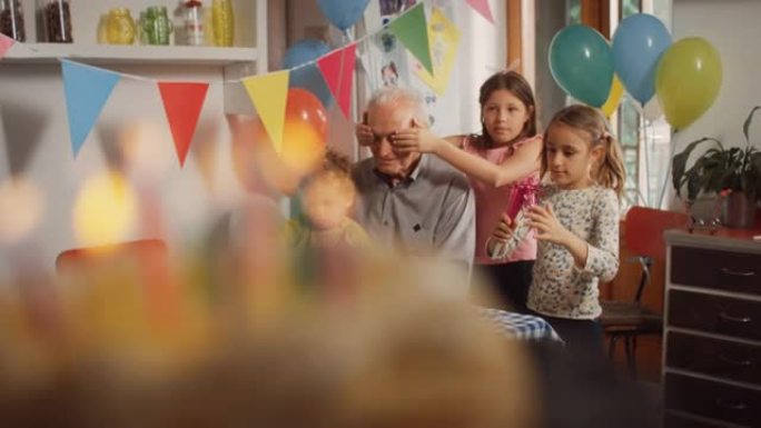 用彩色点燃的蜡烛装饰的生日蛋糕的特写镜头。摄像机运动显示孩子们围着爷爷，遮住了他的眼睛。家庭举行秘密