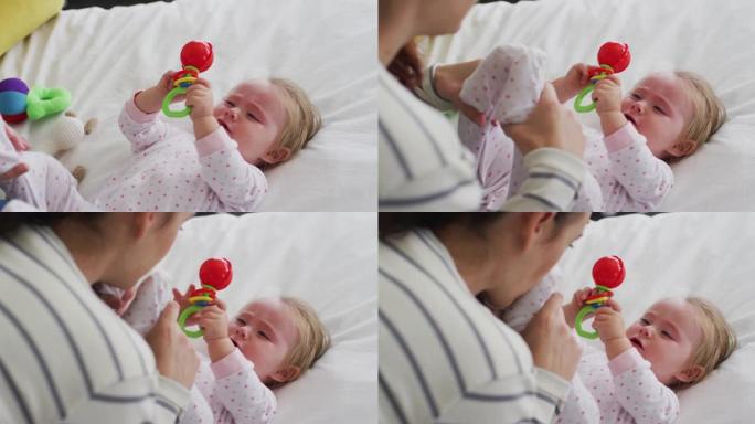 高加索母亲在家里的床上抱着玩具和婴儿玩耍
