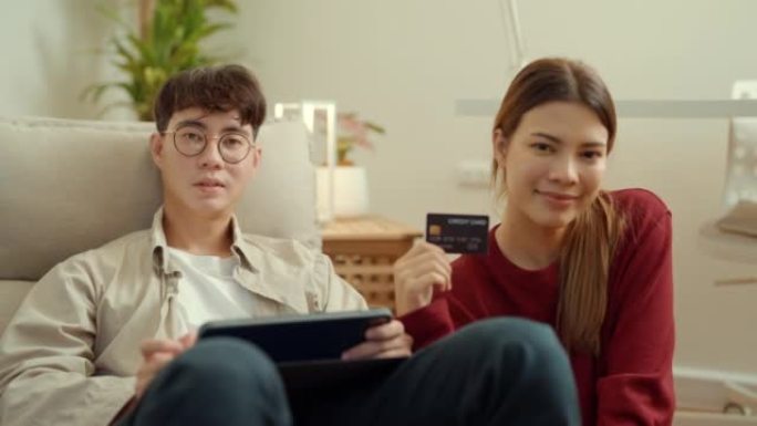 年轻的亚洲夫妇用平板电脑，在家里用送货上门的服务接收包裹。网上购物、移动支付。愉快的购物体验