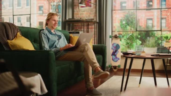 年轻英俊的成年男子坐在阁楼客厅的沙发上，在笔记本电脑上与客户进行视频通话。有创造力的男性在家工作，与