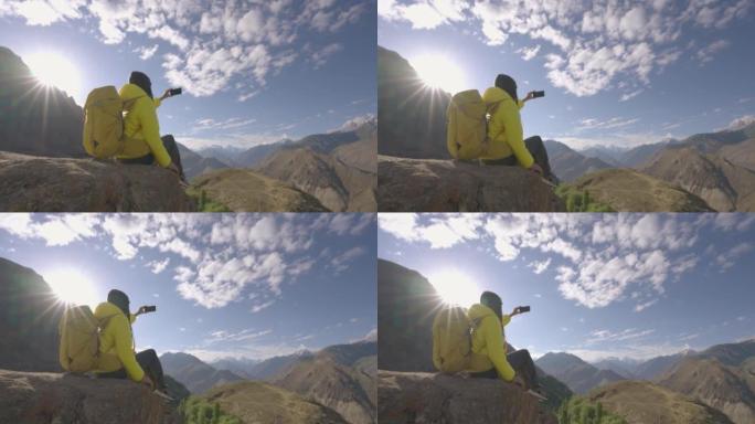 自由旅行者的年轻女性穿着黄色的冬季夹克，背着背包，在早晨的山顶上，用智能手机旅行假期拍摄美丽的景色。